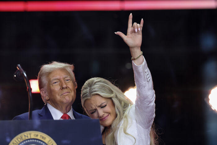 Woman making a hand gesture during a public event, with a man standing beside her, capturing a viral moment on the internet. Woman making a hand gesture during a public event, with a man standing beside her, capturing a viral moment on the internet.