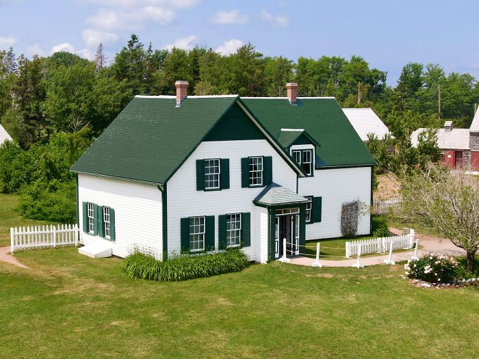 White and green iconic TV house with shutters and chimneys surrounded by a lawn and trees, real life location.