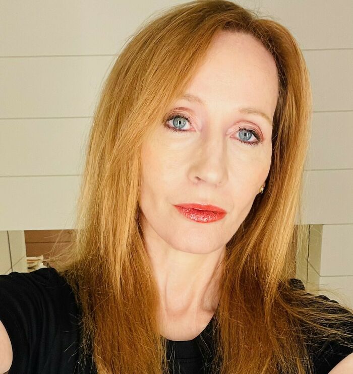 J.K. Rowling with red hair and red lipstick posing indoors, related to her response to Emma Watson in posts. J.K. Rowling with red hair and red lipstick posing indoors, related to her response to Emma Watson in posts.