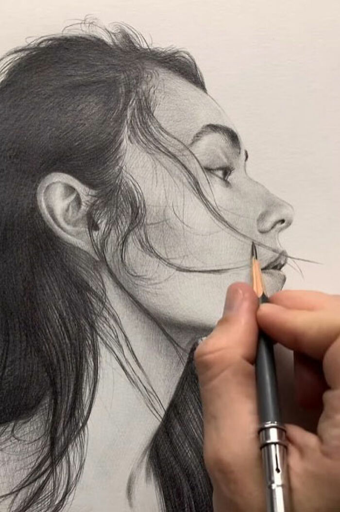 Close-up of a hand creating a pencil portrait that captures every tiny detail of a woman's face and hair.