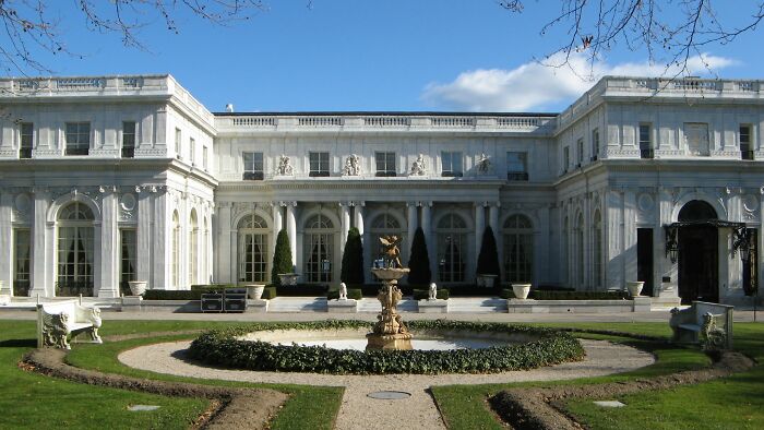 Large iconic TV house with classical architecture, grand fountain, and manicured garden under a clear blue sky.