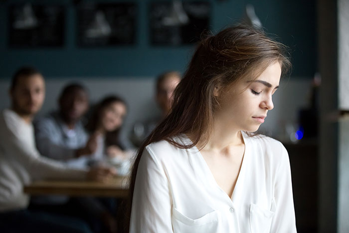 A young woman looking down with sadness while her family sits blurred in the background, symbolizing unwanted siblings adoption. A young woman looking down with sadness while her family sits blurred in the background, symbolizing unwanted siblings adoption.