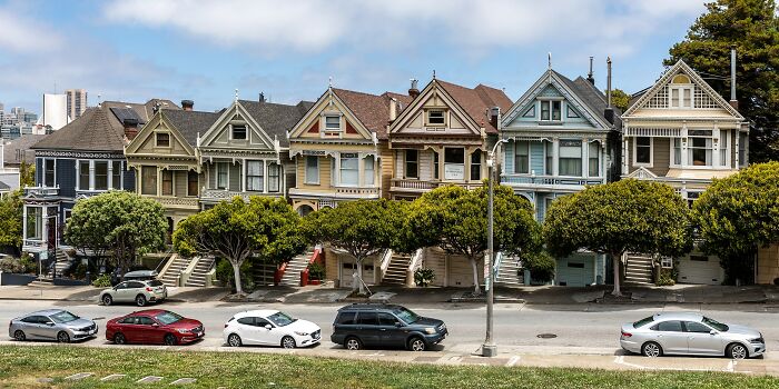 Row of iconic TV houses with distinct colors and architecture, surrounded by trees and parked cars on the street.