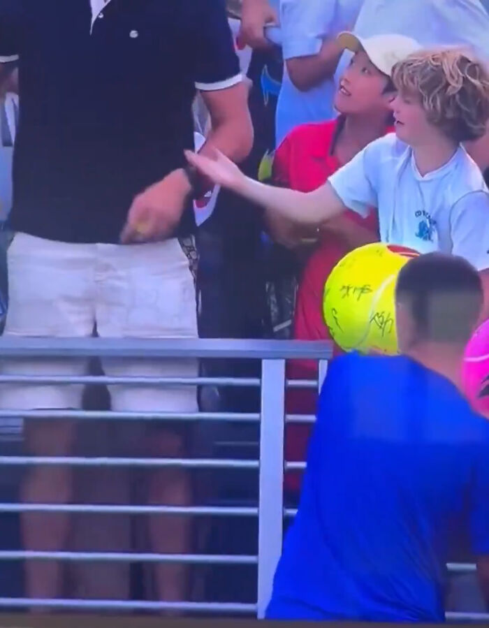 Boy in white shirt reaching out to disgraced CEO who snatched boy's cap at US Open amid crowd and tennis balls. Boy in white shirt reaching out to disgraced CEO who snatched boy's cap at US Open amid crowd and tennis balls.