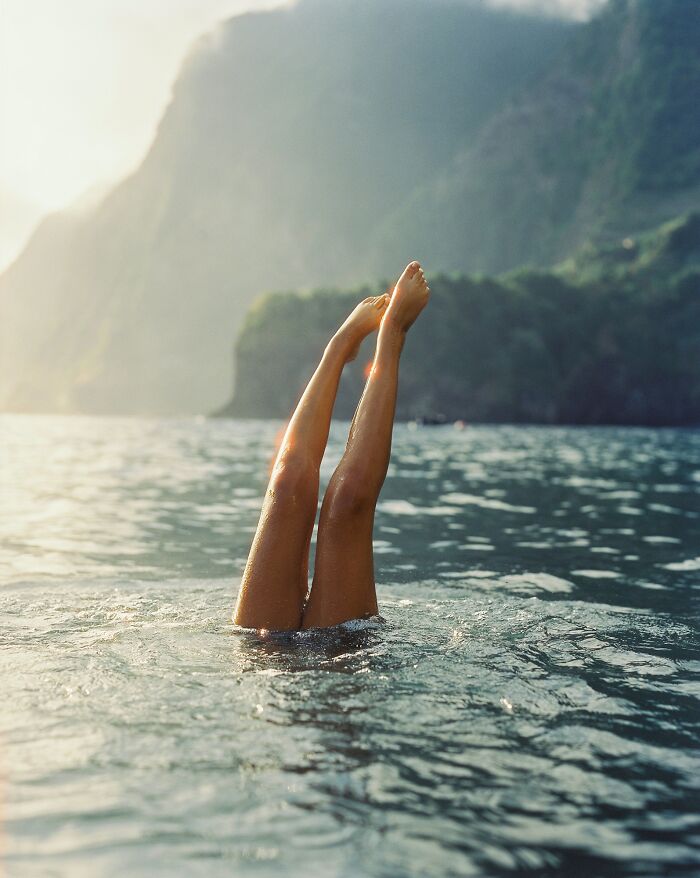 Legs emerging from water with mountain backdrop, captured in analog photo style featured in Analog Sparks Awards.