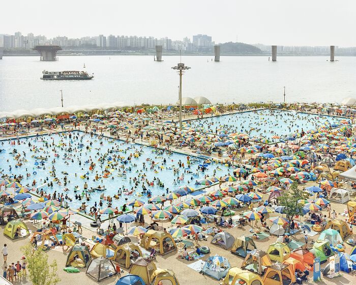Crowded public swimming pools with colorful umbrellas and tents by the river captured in award-winning analog photos.