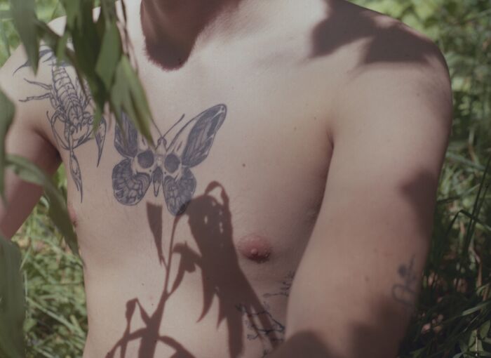 Close-up analog photo of a shirtless person with tattoos and plant shadows, capturing the best of film photography creativity.
