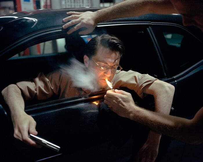 Man in a car lighting a cigarette with a lighter held by another person, captured in an analog photo at night