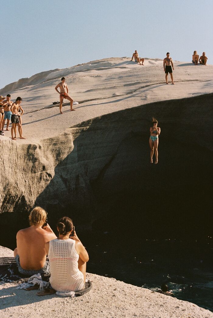 Group of people cliff diving and watching on rocky shore in an analog photo capturing summer moments and excitement.