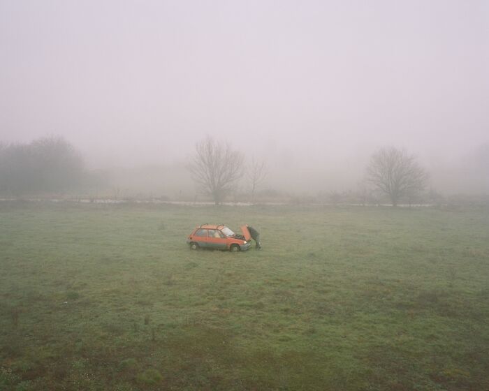 Foggy rural field with a person inspecting an orange car, showcasing the best analog photos from Analog Sparks Awards.