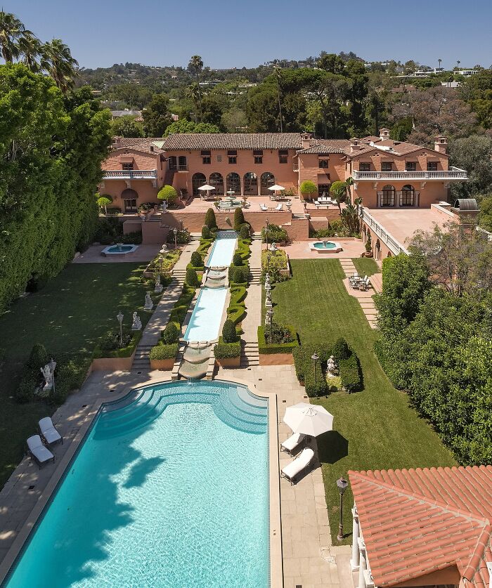 Aerial view of an iconic TV house with a large pool, manicured gardens, and terracotta roof in real life.