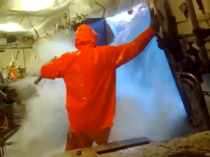 Worker in an orange protective suit handling industrial equipment surrounded by thick smoke in a creepy unsettling job scene