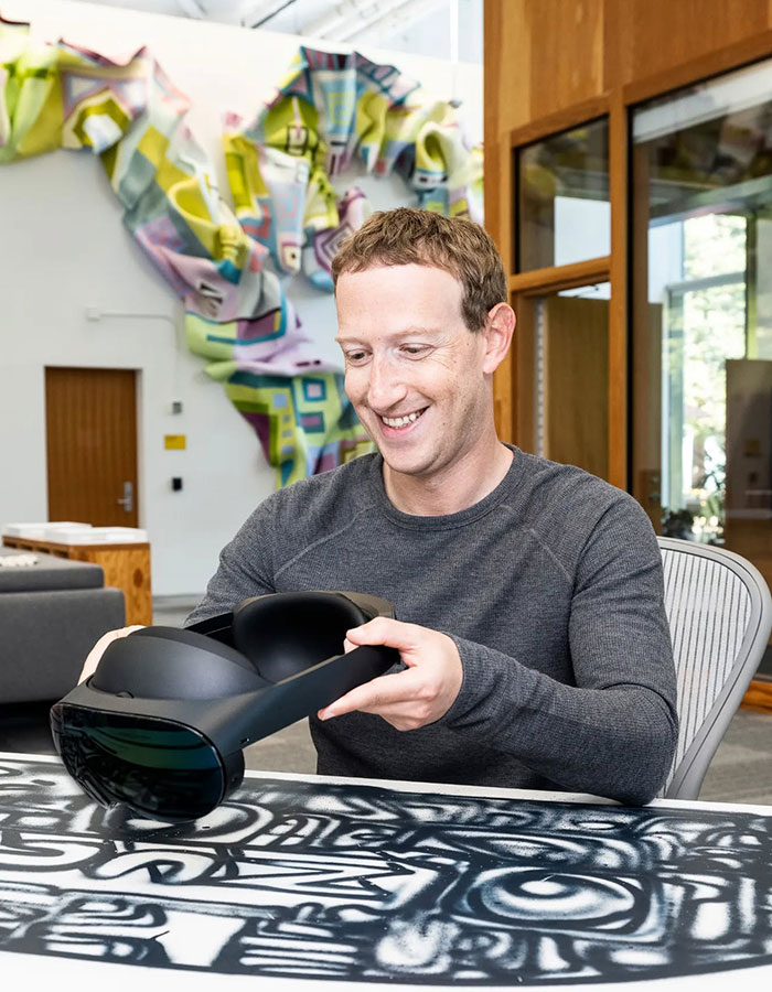 Mark Zuckerberg smiling while holding a VR headset indoors, related to embarrassing hot mic moment with Donald Trump. Mark Zuckerberg smiling while holding a VR headset indoors, related to embarrassing hot mic moment with Donald Trump.