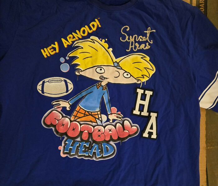 Cartoon character Arnold on a blue Hey Arnold football-themed shirt with text and graphic design elements.