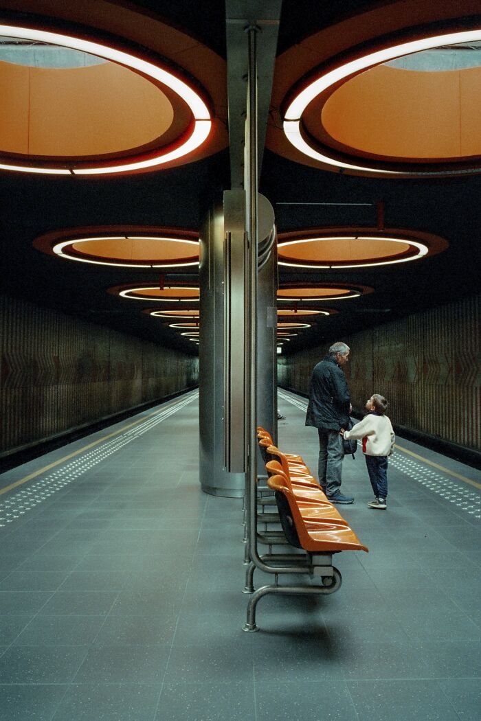 Grandfather and child standing in a subway station with round ceiling lights in an analog photo style.