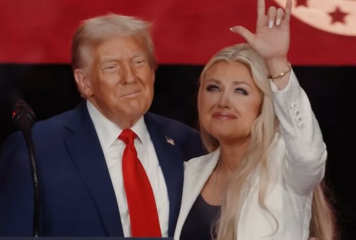 Man in suit and red tie with woman in white jacket waving, related to WWE level stuff and surprise entrance topics. Man in suit and red tie with woman in white jacket waving, related to WWE level stuff and surprise entrance topics.