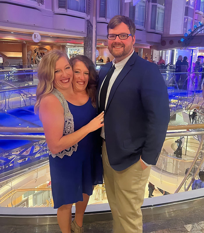 After conjoined twins Abby and Brittany smiling with a man in a formal setting, expert discusses who would be the mom. After conjoined twins Abby and Brittany smiling with a man in a formal setting, expert discusses who would be the mom.