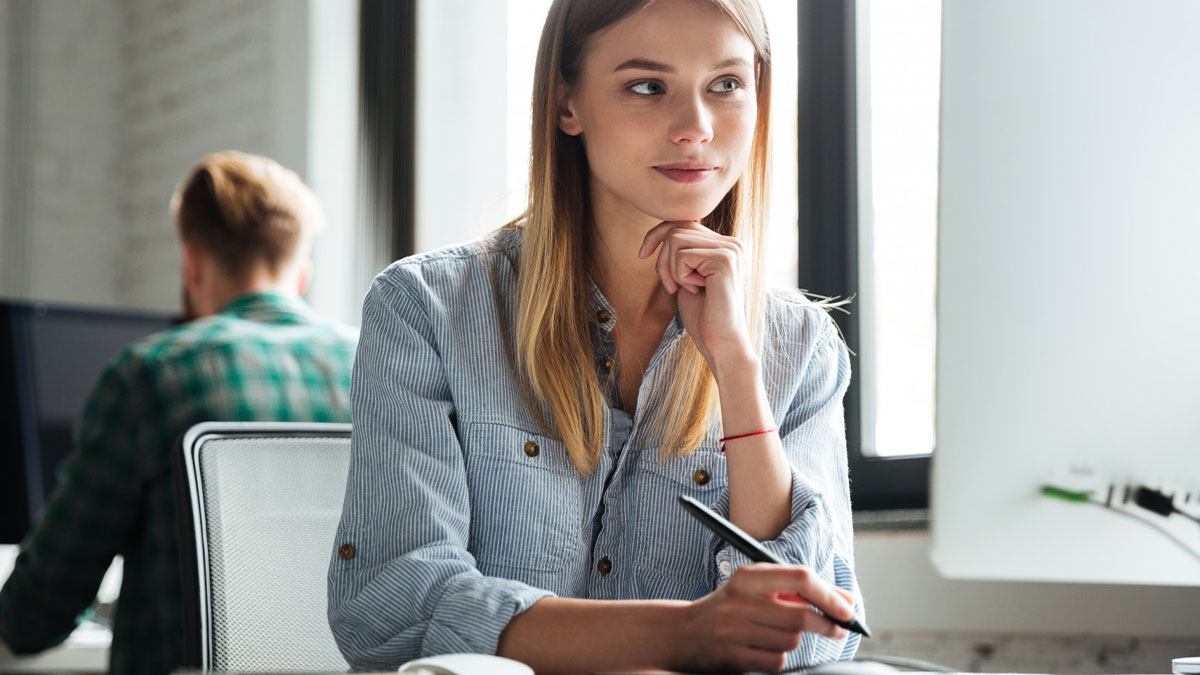 Thoughtful engineer at desk holding pen, reflecting on software access issues and communication with HR team.