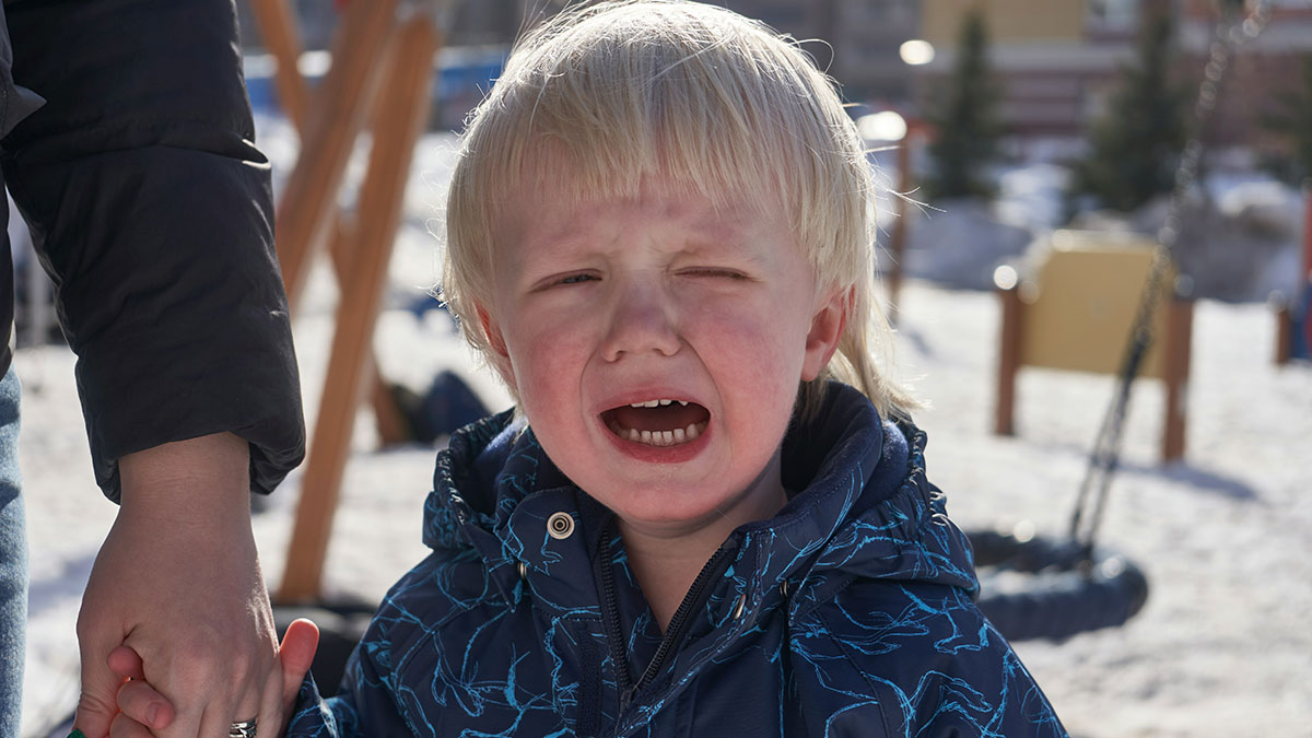 Toddler crying in a park no-walking area, holding adult hand, sparking drama with a livid stranger nearby.