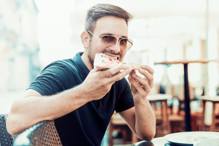 Man enjoying a slice of pizza outdoors, symbolizing life after high school sports glory days for former stars.