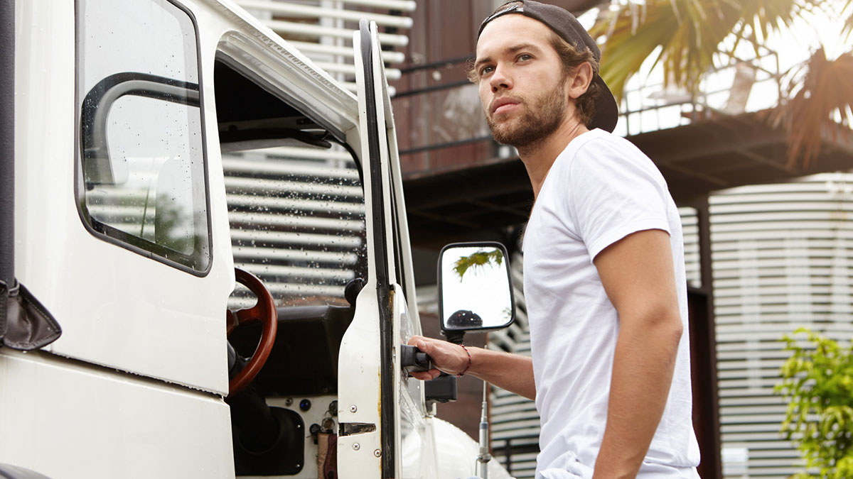 Young man, former high school star, standing by a white truck, reflecting on life after the glory days.