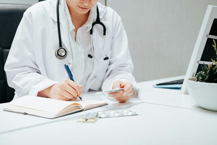 Medical professional with stethoscope writing notes at desk with medication, illustrating suspicious professions concept.