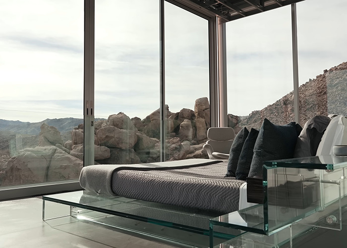 Modern bedroom interior with glass walls featuring rocky desert landscape in the famous invisible house Airbnb owners charge. Modern bedroom interior with glass walls featuring rocky desert landscape in the famous invisible house Airbnb owners charge.