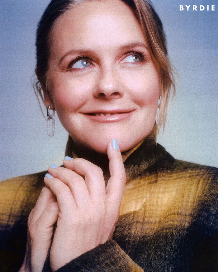 Alicia Silverstone smiling with youthful skin, wearing a plaid jacket and light blue nail polish in a close-up portrait. Alicia Silverstone smiling with youthful skin, wearing a plaid jacket and light blue nail polish in a close-up portrait.