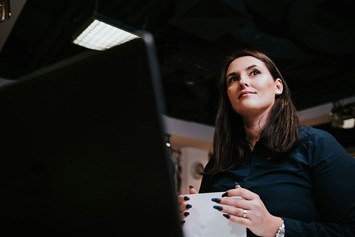 Woman at office desk with dark hair and navy shirt, holding paper, showing a petty response to creepy coworker. Woman at office desk with dark hair and navy shirt, holding paper, showing a petty response to creepy coworker.