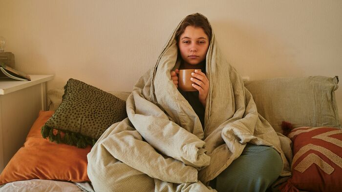 Sick woman wrapped in blanket, holding a mug and looking unsure about attending wedding with positive Covid test. Sick woman wrapped in blanket, holding a mug and looking unsure about attending wedding with positive Covid test.