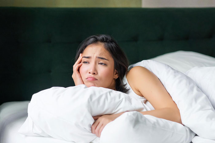 Woman lying in bed looking thoughtful and worried, reflecting on a throuple with anime pillow situation. Woman lying in bed looking thoughtful and worried, reflecting on a throuple with anime pillow situation.