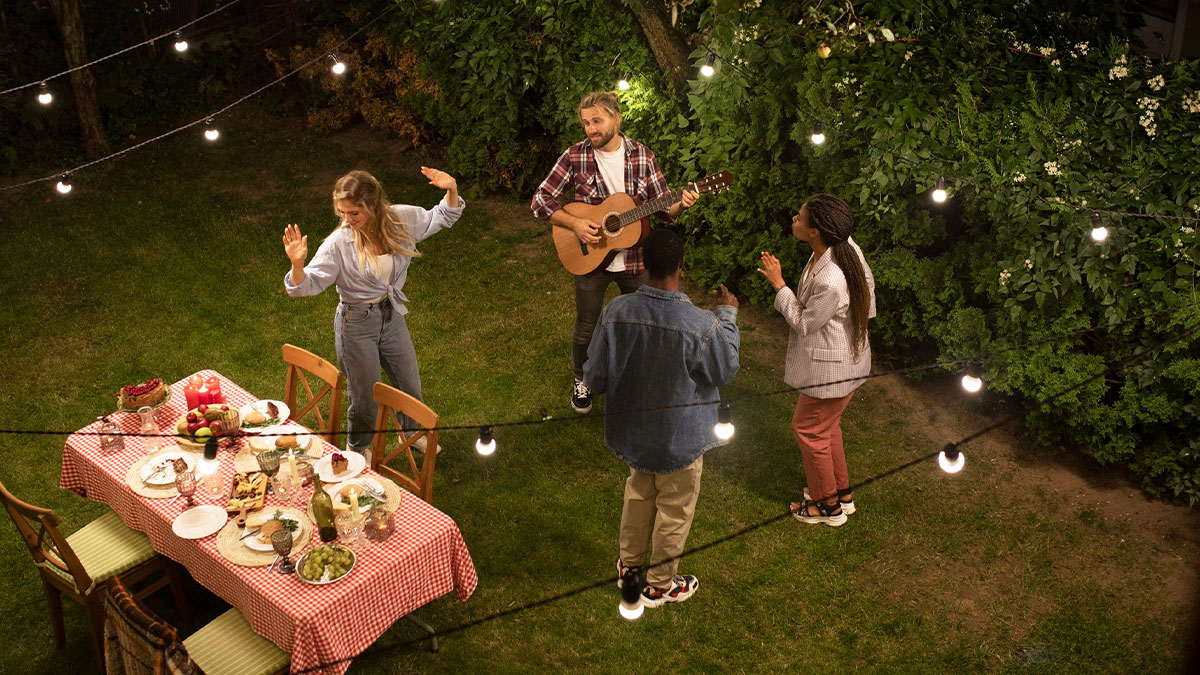 Group of young adults enjoying an outdoor party with guitar music and string lights, highlighting social red flag behavior.