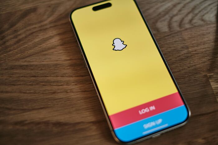 Smartphone displaying Snapchat login screen on wooden table, illustrating childish reasons ladies ditched a guy.