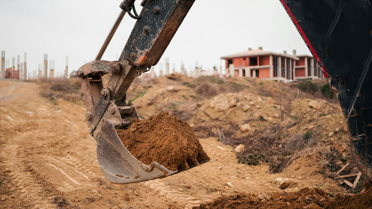 Excavator digging at construction site during archaeological excavation of ancient skeletons buried underground.