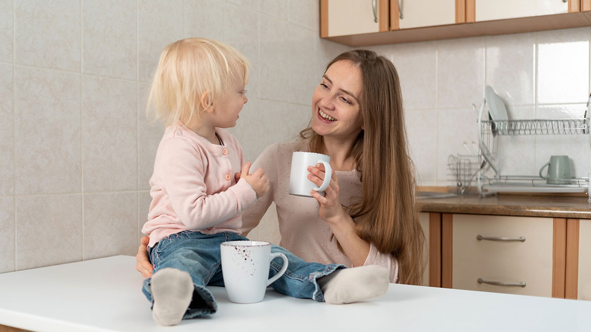 Mother and little girl sitting in kitchen, sharing a moment while holding mugs, highlighting concerns about eating disorder comments.