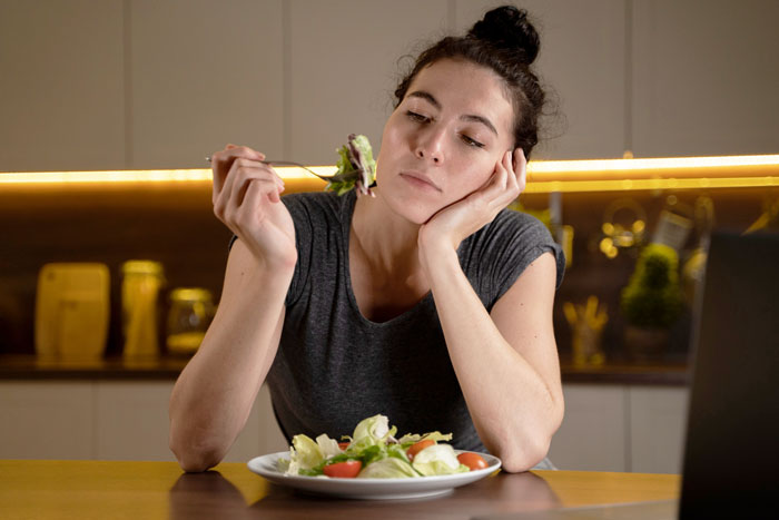 Woman in kitchen looking disinterested at salad, illustrating eating disorder behavior and emotional struggle with food. Woman in kitchen looking disinterested at salad, illustrating eating disorder behavior and emotional struggle with food.