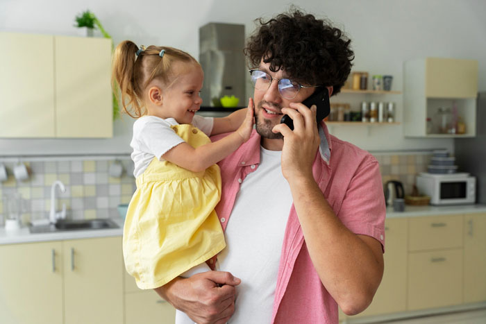 Dad holding little girl in kitchen while talking on phone, concerned about eating disorder comments and child's food aversion. Dad holding little girl in kitchen while talking on phone, concerned about eating disorder comments and child's food aversion.