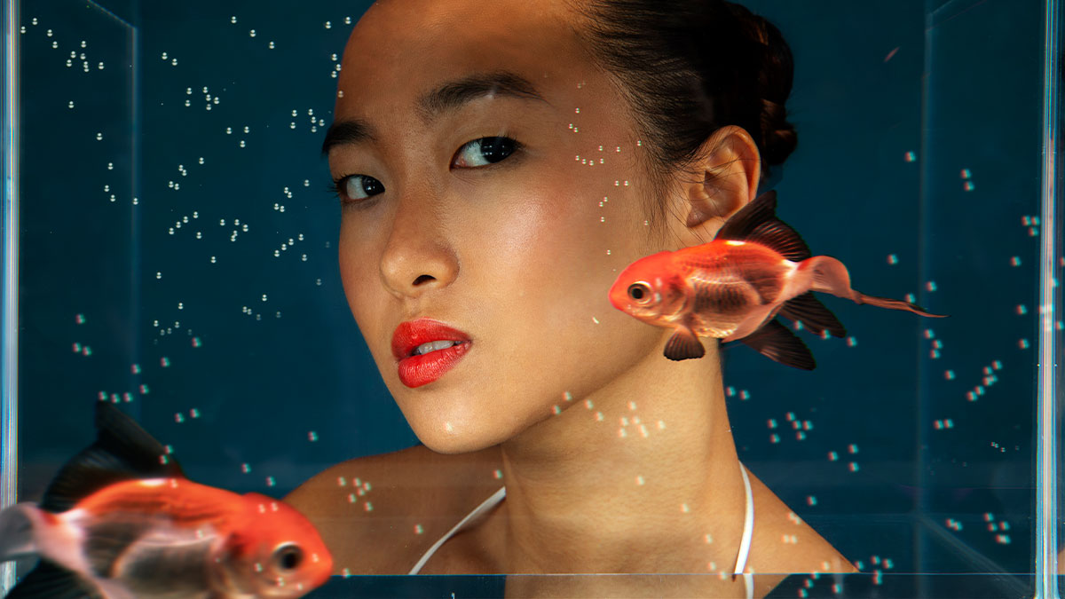 Woman behind aquarium glass with goldfish, illustrating pet store manager defrauds store concept.