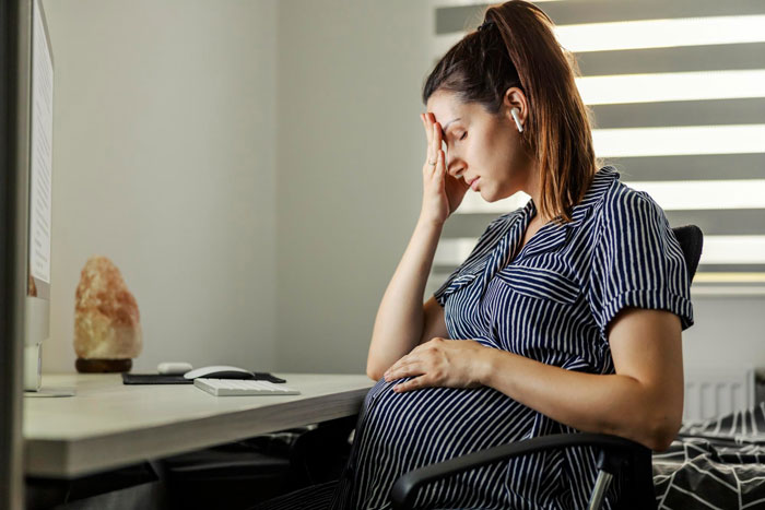 Pregnant woman distressed sitting at a desk, holding her belly and forehead, shocked by hubby’s affair and matching baby name. Pregnant woman distressed sitting at a desk, holding her belly and forehead, shocked by hubby’s affair and matching baby name.