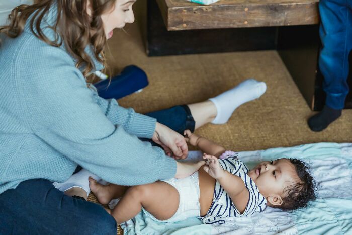 Mom watches as dad takes care of son for the first time while changing his diaper and playing on the floor. Mom watches as dad takes care of son for the first time while changing his diaper and playing on the floor.