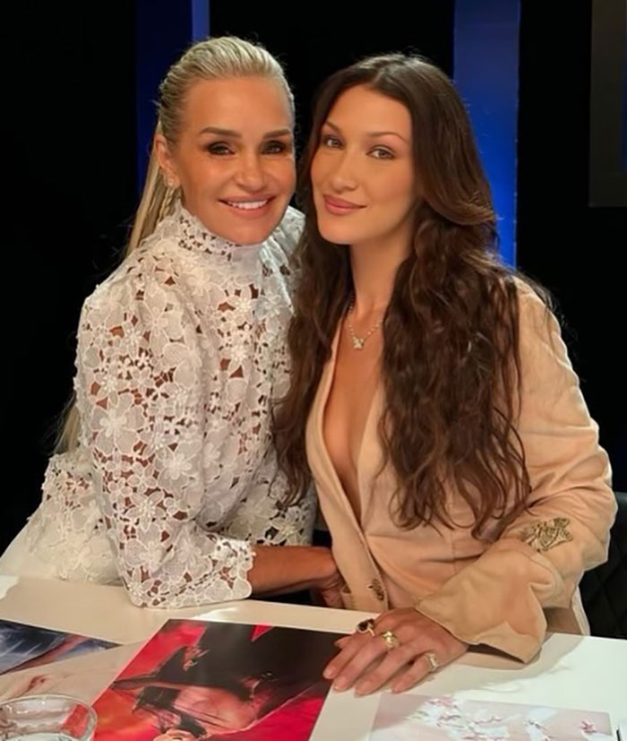 Two women smiling at a table with photos, related to Bella Hadid's hospital posts and years of invisible suffering. Two women smiling at a table with photos, related to Bella Hadid's hospital posts and years of invisible suffering.