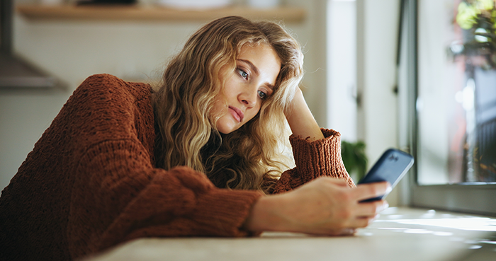 Young woman in a brown sweater looking sadly at her phone, depicting long-distance romance struggles and relationship scandal. Young woman in a brown sweater looking sadly at her phone, depicting long-distance romance struggles and relationship scandal.