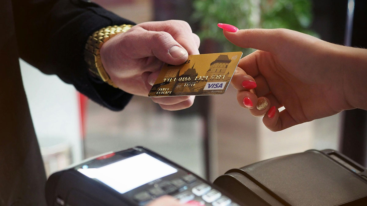 Man handing a credit card to a woman with pink nails during a first date at a payment terminal.
