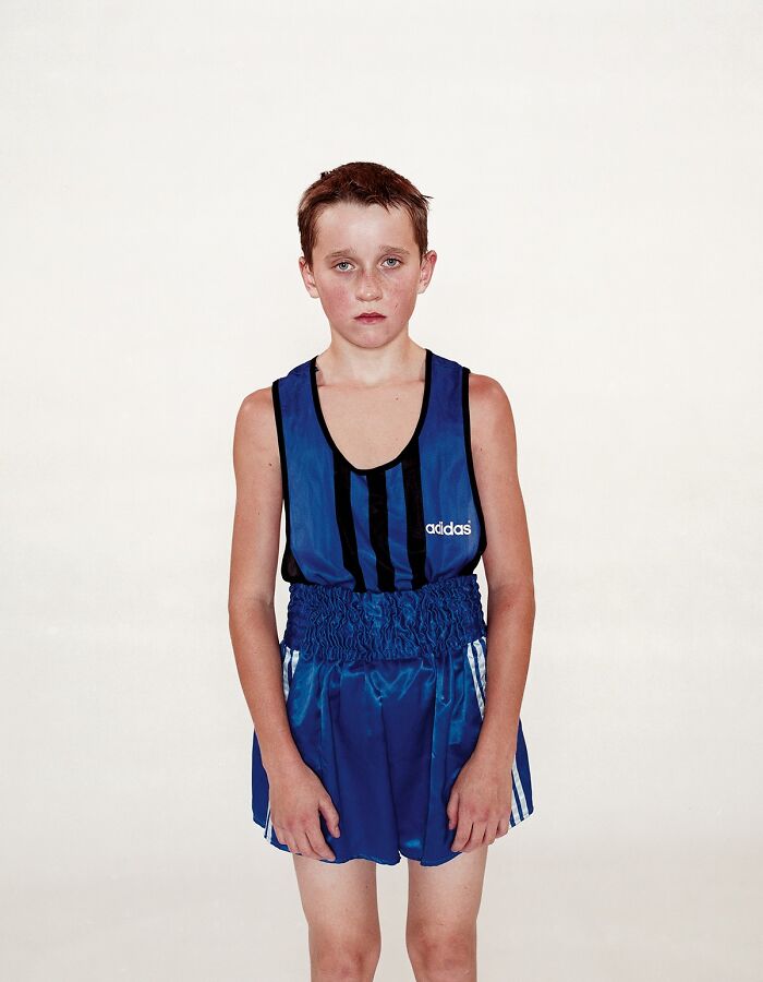 Young boxer standing in blue Adidas boxing outfit with hand wraps before their first match, looking serious and focused.