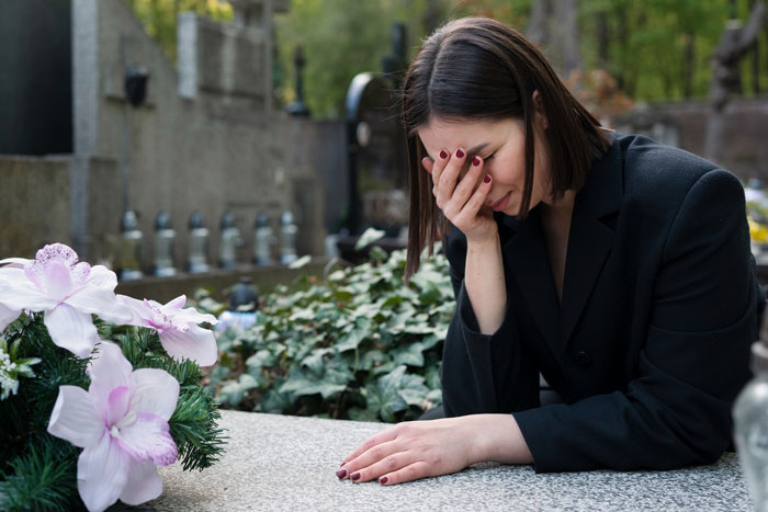 Woman grieving at a gravesite, emotionally covering her face while reflecting on her boyfriend who died and friend messaging experiences.
