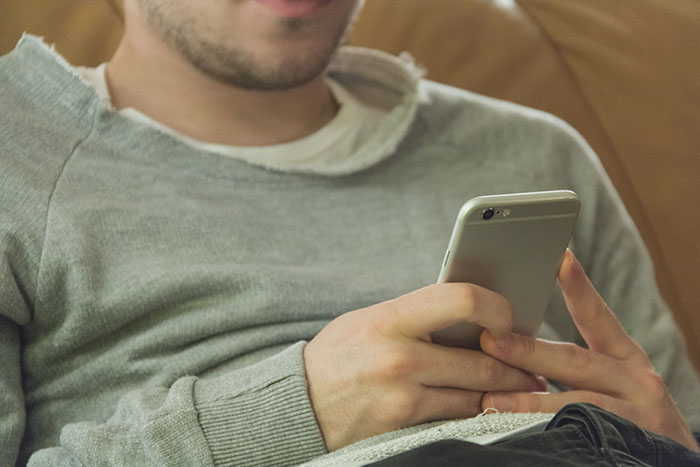 Man in casual grey sweater holding a smartphone, representing a hidden device found in closet prank by boyfriend. Man in casual grey sweater holding a smartphone, representing a hidden device found in closet prank by boyfriend.