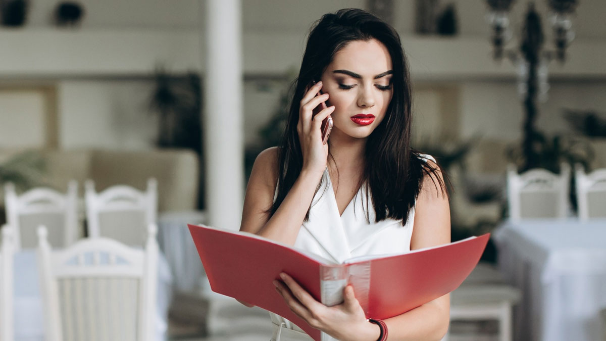 Bride looking concerned while on phone reviewing wedding seating chart in a decorated venue, showing trust and loyalty conflict.