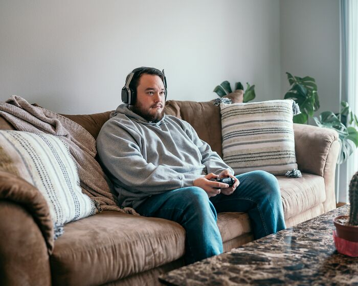 Adult man wearing headphones playing video games on a couch, illustrating adults who failed to understand growing up is mandatory.