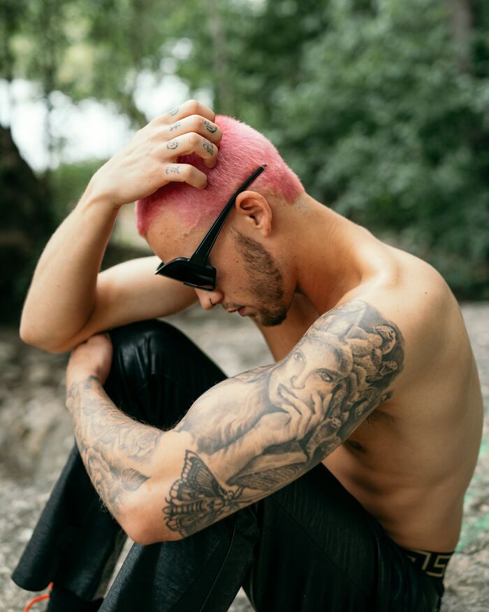 Man with pink hair and extensive detailed tattoos on his arm, showing examples of client tattoo requests.