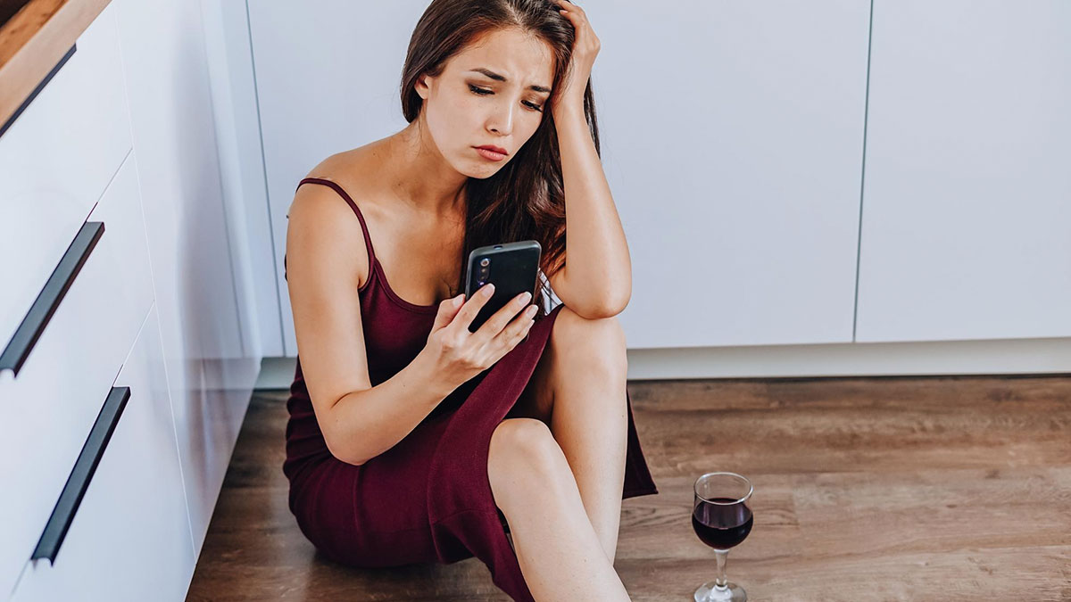 Woman sitting on floor looking at phone upset after boyfriend ditches plans last minute, leading to fast breakup.